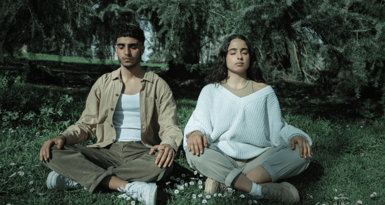 Two people meditating outdoors on grass, calm and grounded — healing and self-care